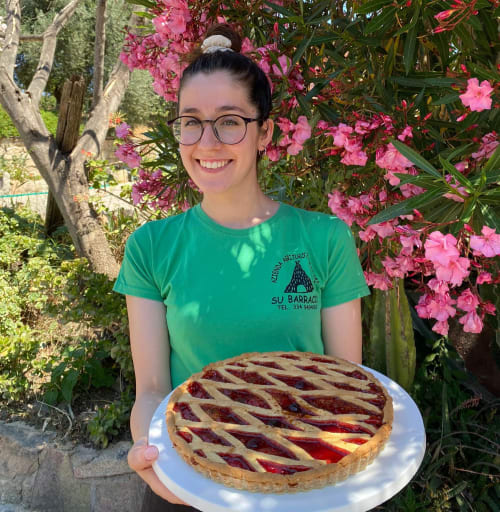 Staff member at Agriturismo Su Barraccu holding homemade berry tart among pink flowers