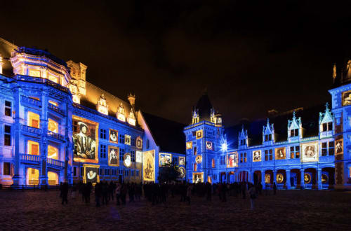 La place du château de Blois illuminée la nuit avec des projections lumineuses bleues et dorées sur les bâtiments historiques de la Renaissance