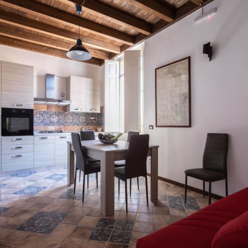 Cucina-sala da pranzo moderna con travi in legno, mobili bianchi, rivestimento di piastrelle blu, sedie da pranzo scure e opere d'arte incorniciate