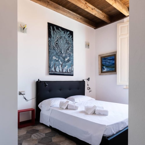 Camera moderna presso la Maison Belle Époque a Oristano con letto imbottito nero, biancheria bianca, travi di legno a vista e quadri incorniciati