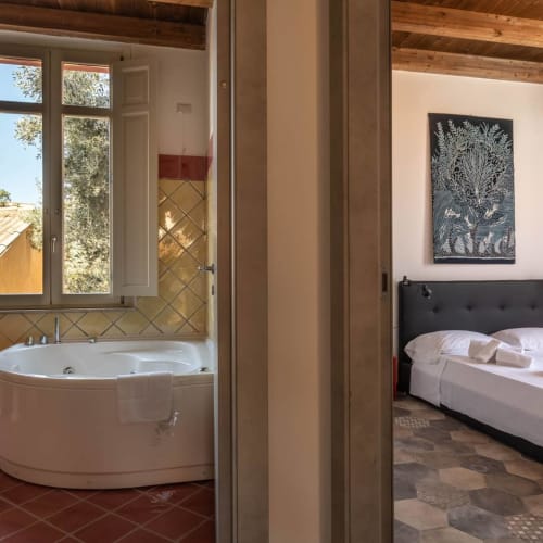 Camera da letto con bagno ensuite con vasca idromassaggio, travi in legno e vista sulla piscina di Maison Belle Époque, Oristano