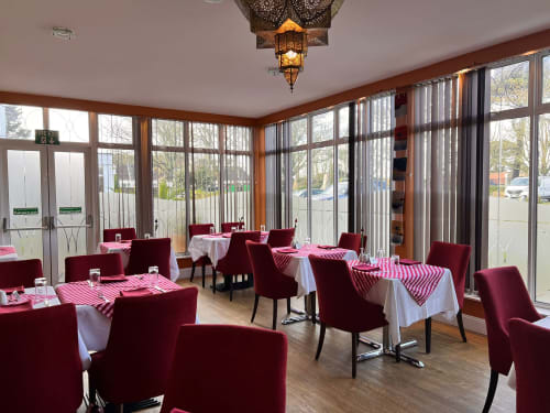 Salle à manger de l'Hôtel La Trelade avec chaises bordeaux, nappes blanches et baies vitrées donnant sur les jardins de St