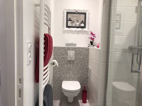 Salle de bains moderne à la Conciergerie Des Climats à Beaune avec carrelage blanc, mosaïque grise, WC mural et radiateur sèche-serviettes