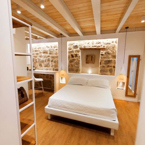 Camera moderna in stile ecodesign dell'hotel a Olbia con letto bianco, travi in legno, muri in pietra e illuminazione a sospensione presso In Centro