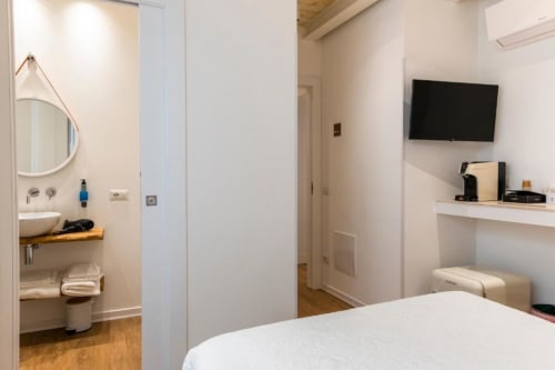 Modern hotel bedroom at In Centro Da Viola featuring white walls, wooden floors, flat-screen TV, and en-suite bathroom with