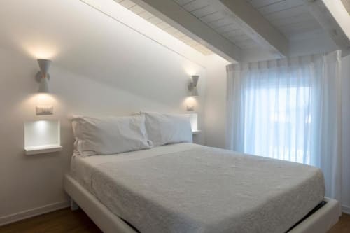 Modern bedroom at In Centro Da Viola with white bed, wall sconces, and natural light in Olba