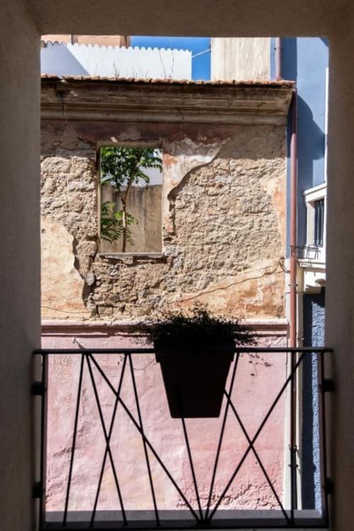 Balcony view of historic stone building in Olbia with potted plant and wrought iron railing at In Centro Da Viola hotel