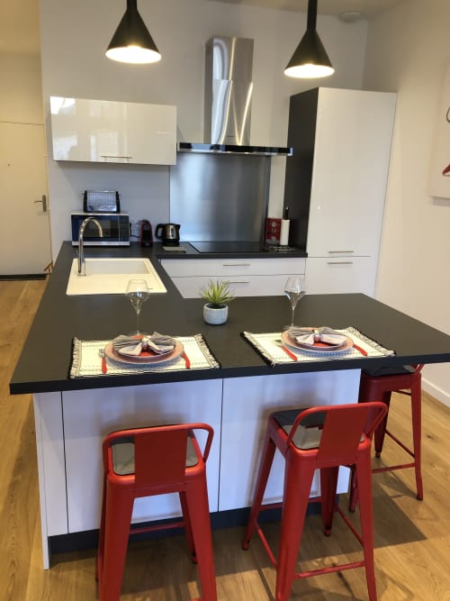 Cuisine et salle à manger modernes dans un appartement de Beaune avec plans de travail noirs, placards blancs, tabourets rouges et couverts