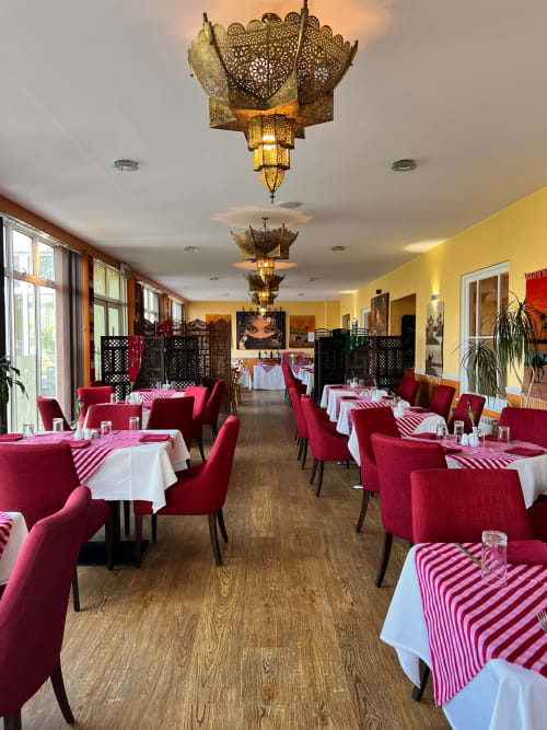 Salle à manger de l'hôtel La Trelade avec chaises rouges, linges à rayures roses, lustres en laiton ouvragé, murs jaunes, Saint-Martin