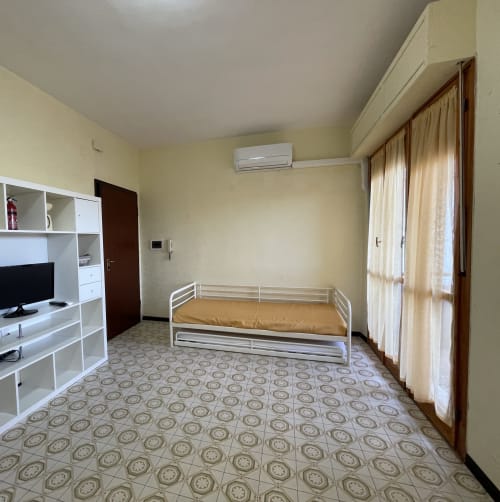 Camera da letto spaziosa alle Rigiariloo Home Apartments con letto singolo, scaffalature bianche, TV e vista sul giardino