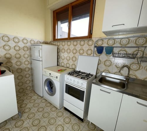 Cucina con rivestimento in piastrelle beige, elettrodomestici bianchi, fornello a gas e lavatrice presso Rigiariloo Home Apartments, San Giacomo degli