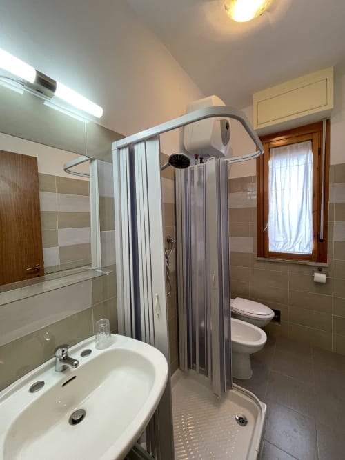 Bagno moderno negli Appartamenti Rigiariloo con cabina doccia, lavabo bianco, wc e piastrelle a righe