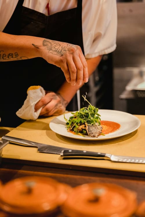 Chef dressant un plat gastronomique avec verdure et sauce orange au Chalet Mont-Blanc, Chamonix