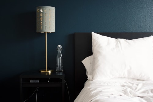 Chambre minimaliste au Chalet Mont-Blanc : tête de lit foncée, oreillers blancs, lampe dorée sur table de nuit noire, mur bleu-vert