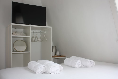 Suíte moderna do VAGO Alcântara Suites em Lisboa com toalhas brancas enroladas na cama, TV na parede e armazenamento branco