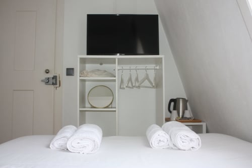 Quarto moderno do VAGO Alcântara Suites Lisboa com toalhas brancas enroladas na cama e prateleiras de armazenamento com TV