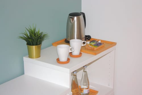 Minibar do quarto de hotel com chaleira elétrica, canecas brancas, porta-copos laranja, planta em vaso e seleção de chás no VAGO