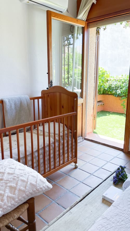 Cuna de madera en dormitorio luminoso con suelo de terracota y acceso al jardín en Casa Rural Villa del Jerte