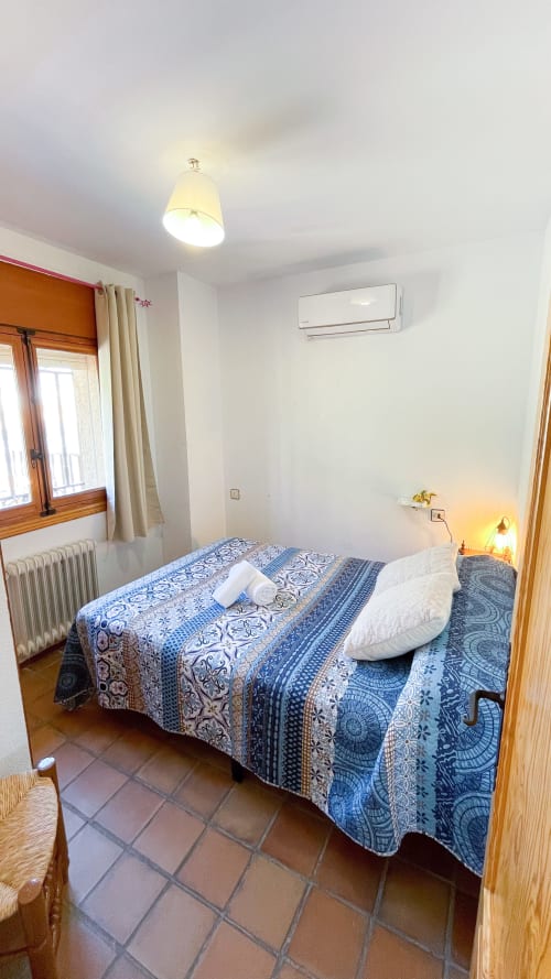 Dormitorio luminoso en Casa Rural Villa del Jerte con ropa de cama de patrón azul, muebles de madera y aire acondicionado en El Torno