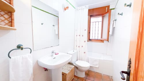 Baño luminoso con azulejos blancos, lavamanos de pedestal, inodoro y ducha en villa Casa Rural Villa del Jerte