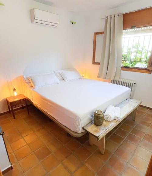 Dormitorio luminoso en Casa Rural Villa del Jerte con ropa de cama blanca, banco de madera, azulejos de barro y vistas a las montañas