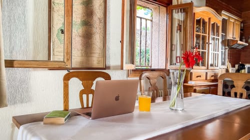 Espacio de trabajo moderno en Casa Rural Villa del Jerte con portátil, zumo de naranja y flores rojas con vistas a las montañas