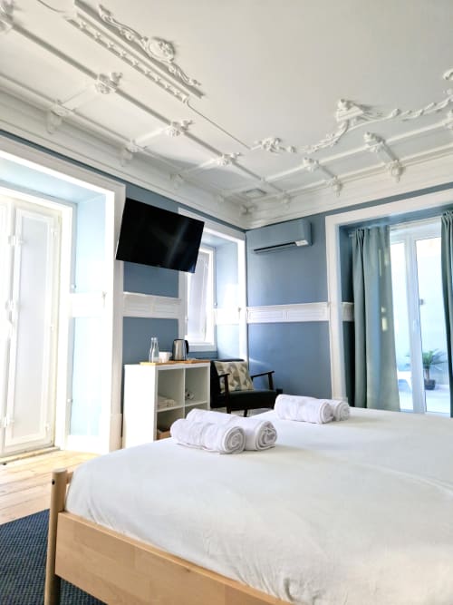 Suíte luminosa no VAGO Alcântara com cama de madeira, roupas de cama brancas, paredes azuis, TV de tela plana e vista para o terraço em Lisboa