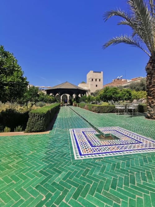 Traditional Moroccan riad courtyard with green zellige tiles, central fountain, and arched pavilion in Marrakesh