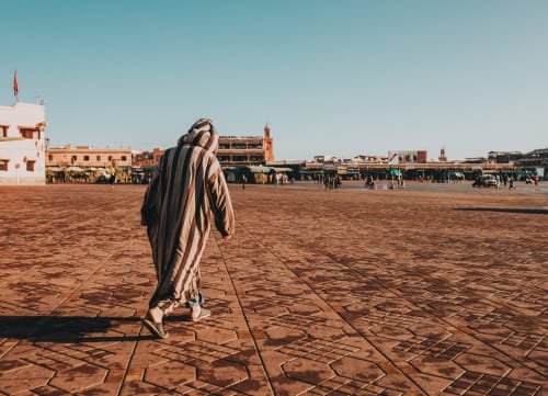 Person in striped djellaba walking across Jemaa el-Fnaa square in Marrakesh, Morocco