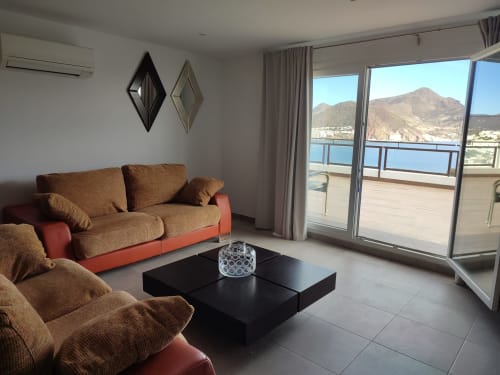Moderna sala de estar en El Faro De Los Genoveses con vistas al mar, sofá marrón, mesa negra y montañas costeras visibles