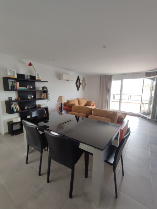 Moderno apartamento con vistas al mar en San José, Almería. Cuenta con comedor, sofá beige, estanterías negras y acceso a balcón.