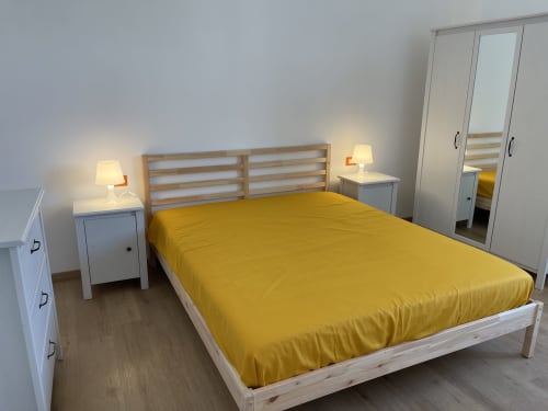 Camera luminosa presso Rigiariloo Home Apartments con piumino giallo, letto in legno, comodini con lampade e specchio