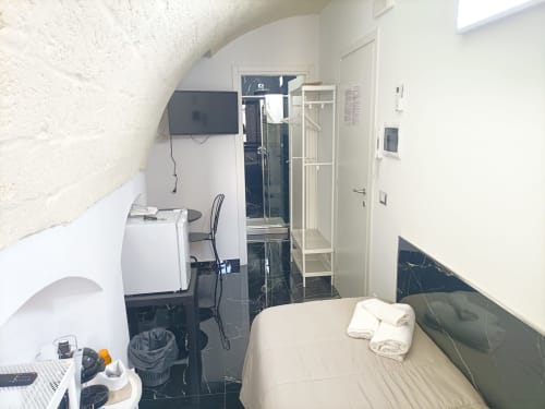 Compact hotel room at Newhouse Bari with bed, TV, shower room, and black marble flooring
