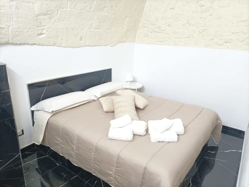 Camera moderna dell'hotel Newhouse Bari con biancheria beige, pavimento in marmo nero, cuscini bianchi e testiera scura