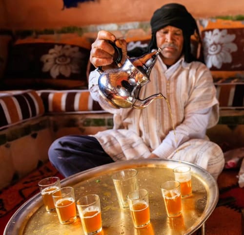 Hôte berbère versant le thé à la menthe traditionnel, avec des verres sur une table en laiton