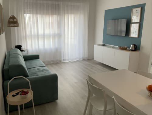 Modern living room in Lamar Suites Seafront Apartments with green sofa, white dining table, and teal accent wall with TV,