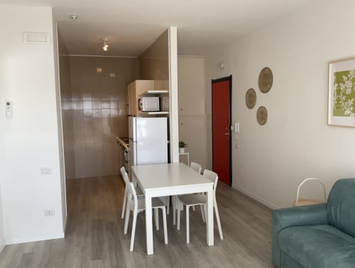 Modern apartment living area with white dining table, kitchenette, and teal sofa at Lamar Suites Seafront in Misano Adriatico
