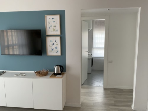 Modern apartment living room at Lamar Suites with teal accent wall, flat-screen TV, white cabinetry, and doorway to kitchen