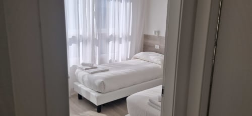 Modern bedroom in Lamar Suites Seafront Apartments with white bed, sheer curtains, and harbour view in Misano Adriatico