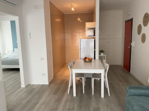 Modern apartment dining area with white table, kitchen with orange-tiled backsplash, and view to bedroom at Lamar Suites