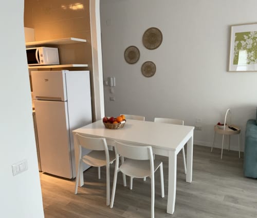 Modern apartment kitchen and dining area at Lamar Suites Seafront Apartments with white table, refrigerator, and decorative