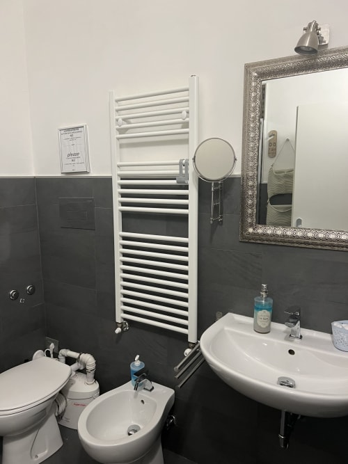 Modern bathroom at Casa Castagna B&B in Salerno with white radiator, round mirror, dual sinks, and black tiled walls
