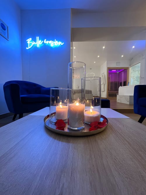 Au premier plan, trois bougies allumées sur une table basse. Au second plan, le néon Bulle évasion à gauche et un sauna à droite.