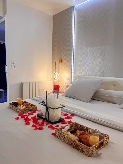 Deux plateaux petit-déjeuner sur un lit décoré avec des pétales de roses rouges et un cœur blanc.