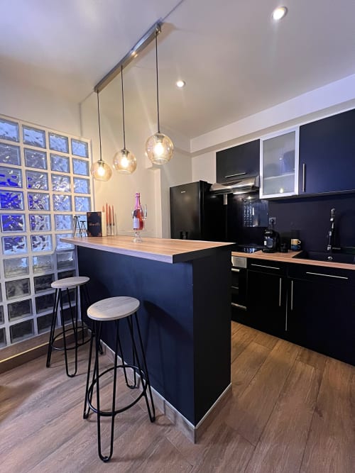 Cuisine lumineuse équipée de meubles noirs. Un bar et deux tabourets. Trois luminaires suspendus.