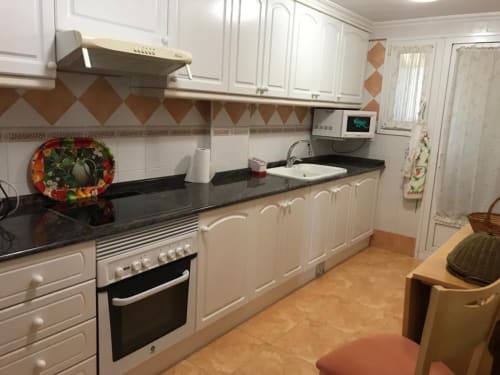 Modern kitchen in Retiro Playa & Spa Apartment, Almagro, with white cabinets, black countertops, and orange tile flooring