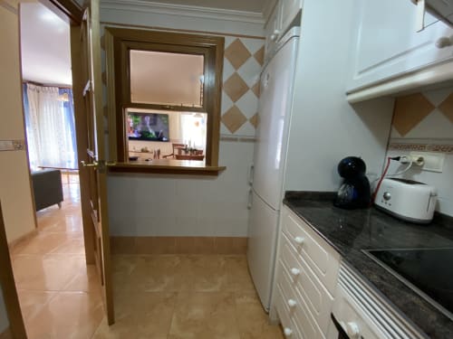 Modern kitchen in Retiro del Teatro apartment, Almagro, with white cabinetry, dark countertops, and dining area access