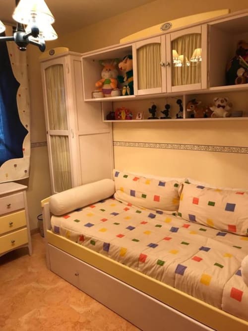 Bright children's bedroom with cream sofa bed, colorful patterned bedding, wall-mounted storage cabinets, and toys at Retiro