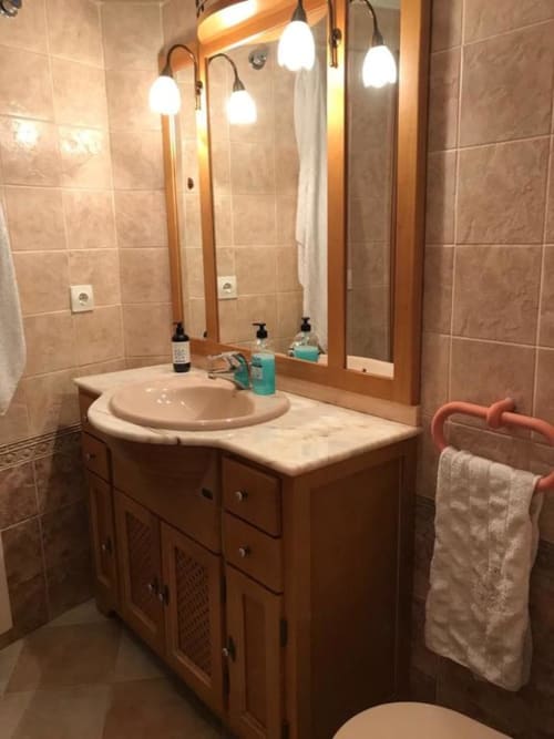 Modern bathroom with wooden vanity, round sink, illuminated mirror, and beige tile walls in Retiro del Teatro apartment,