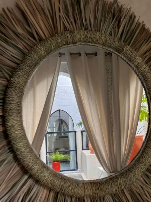 Circular woven mirror framing view of Riad Palau Marrakech terrace with curtains and courtyard